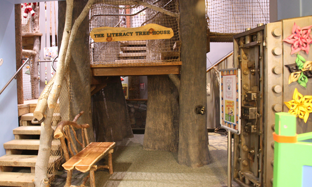 Exhibit of Literacy Tree House with stairs leading to rope netted platform.