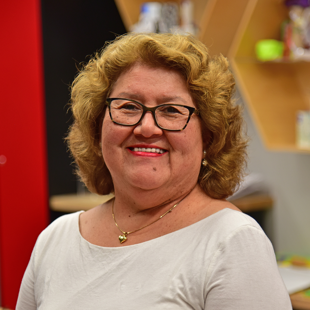 Carmen Neale Woman with curly blonde hair and white shirt and dark-rimmed glasses smiling
