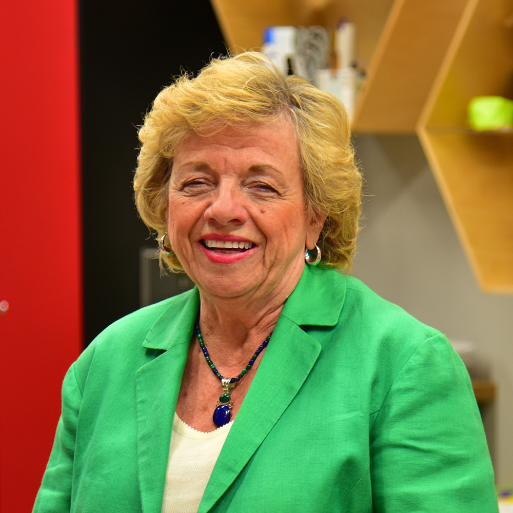 Woman with blond hair wearing a green jacket over a white shirt smiling