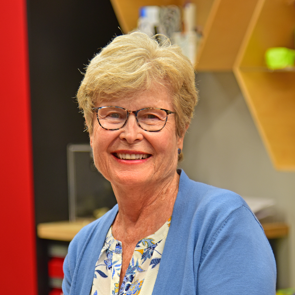 Cathleen Schmitz Woman with blond hair and dark-rimmed glasses wearing a blue sweater over a white flowered shirt smiling