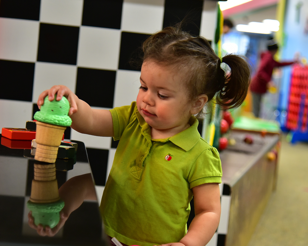 Young girls with brown hair and pigtails wearing lime-green polo shirt playing with plastic ice cream cone