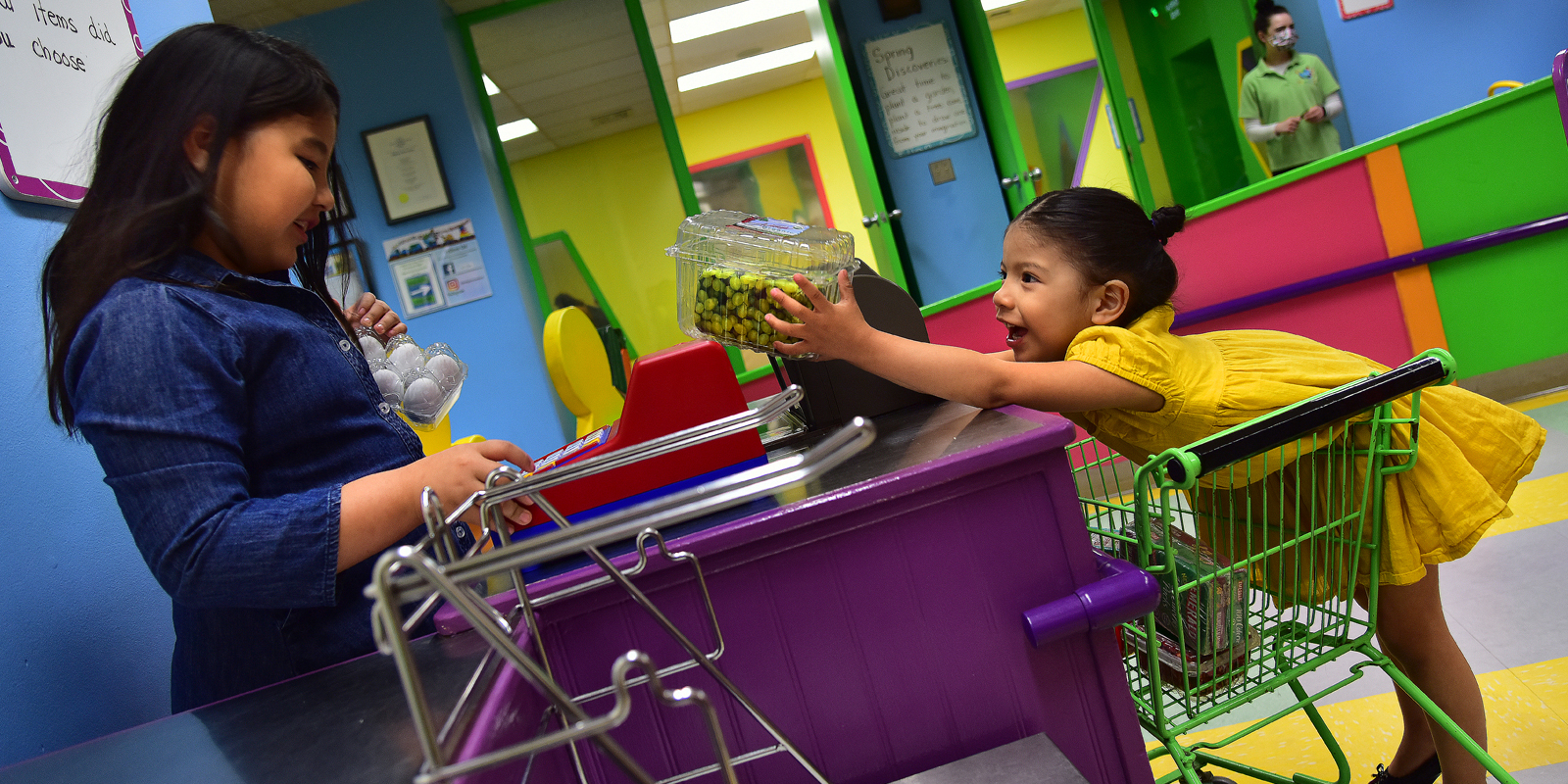 Two young girls with dark hair playing at a pretend grocery store checkout
