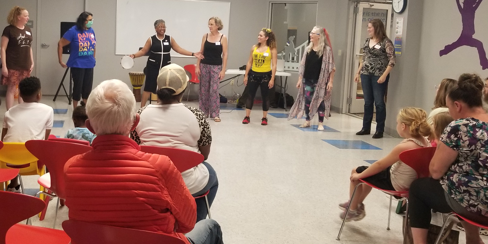 Several women standing in front of small audience with one woman holding tambourine