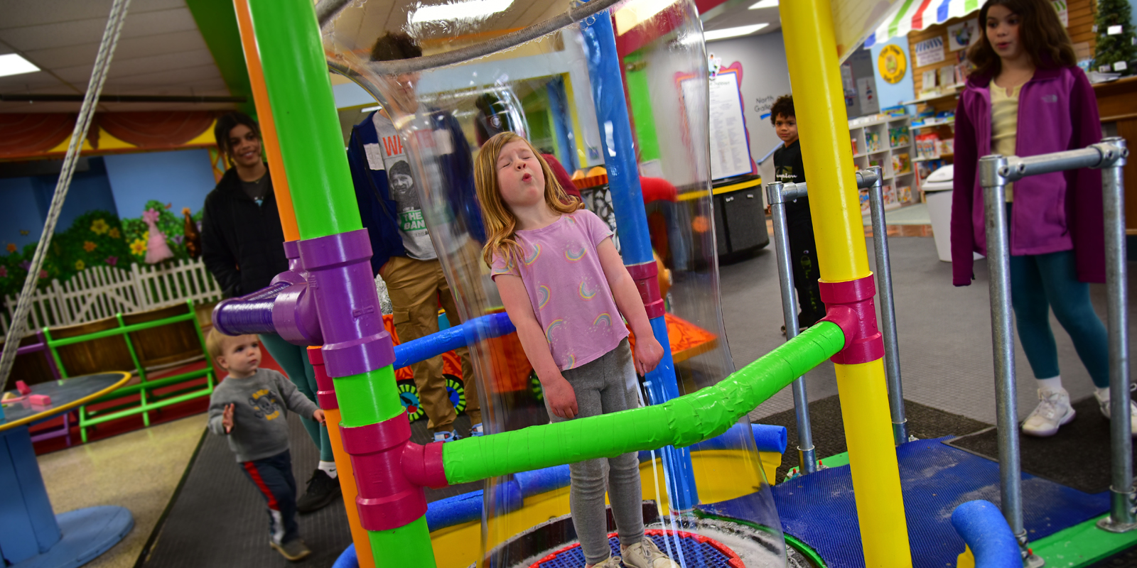Young girl with blonde reddish hair standing with eyes closed inside a large bubble