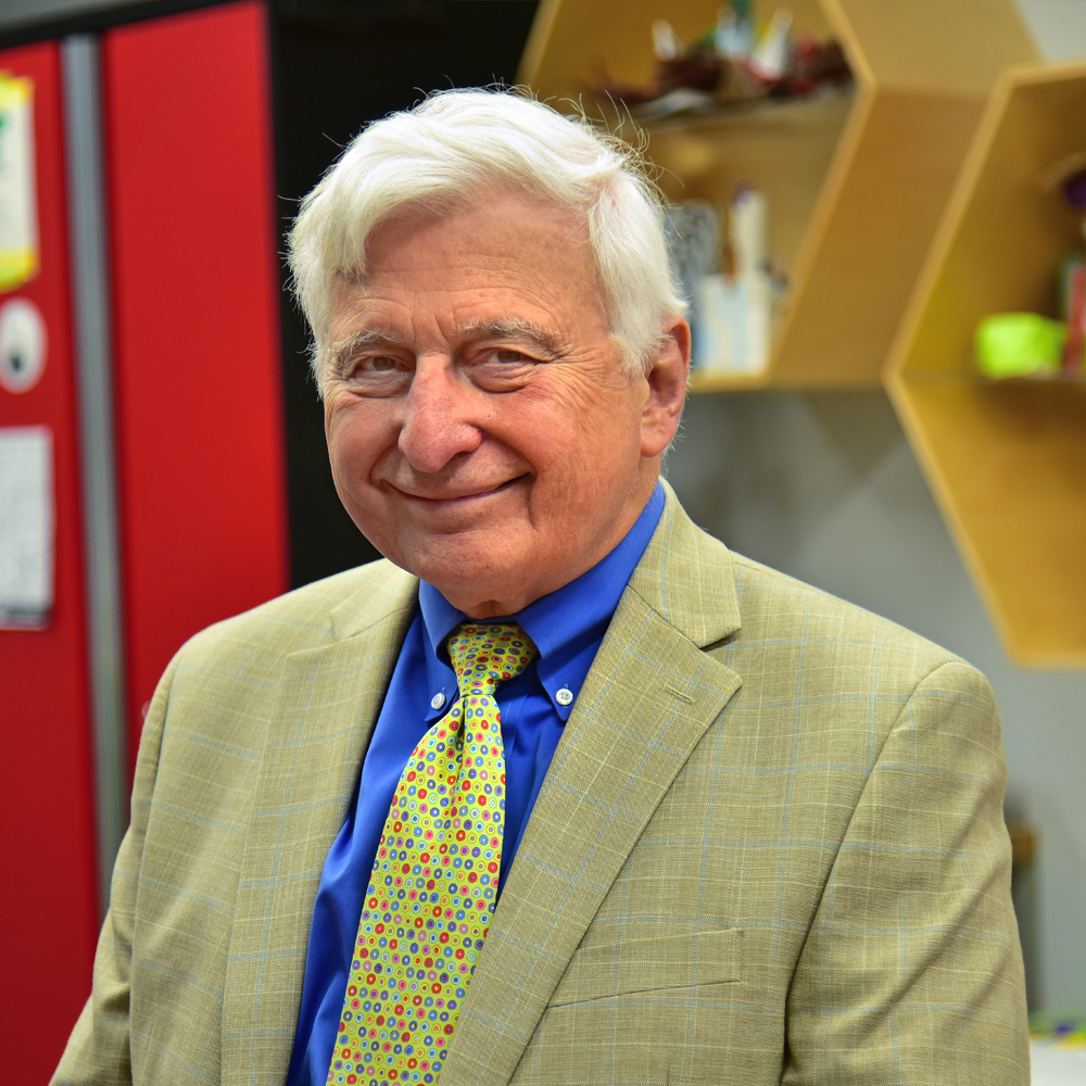 Kenneth Merz Man with white hair wearing a green and blue checkered sports coat over a blue dress shirt and green dotted tie smiling.