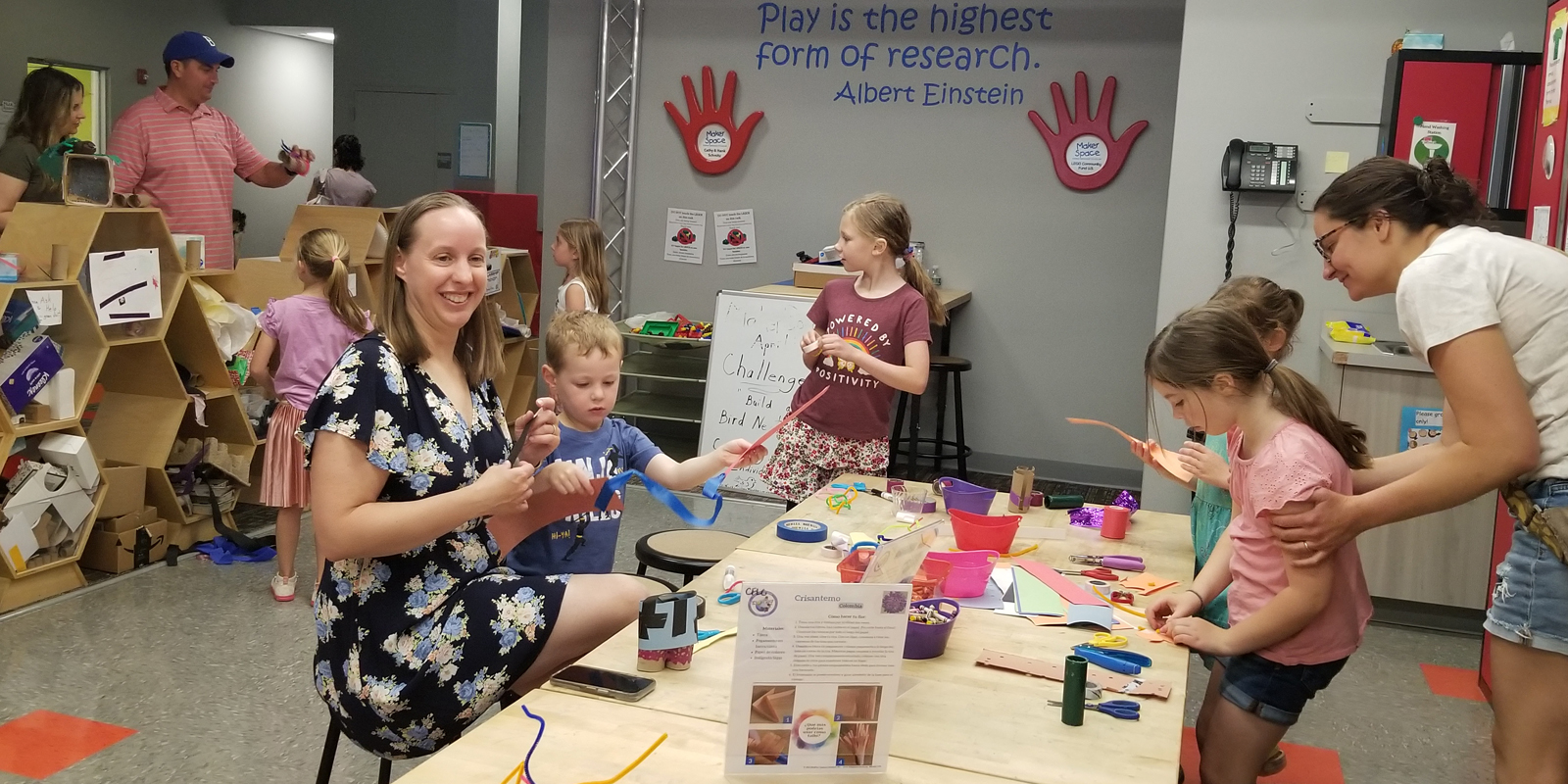 Parents and children standing around a long table doing arts and crafts