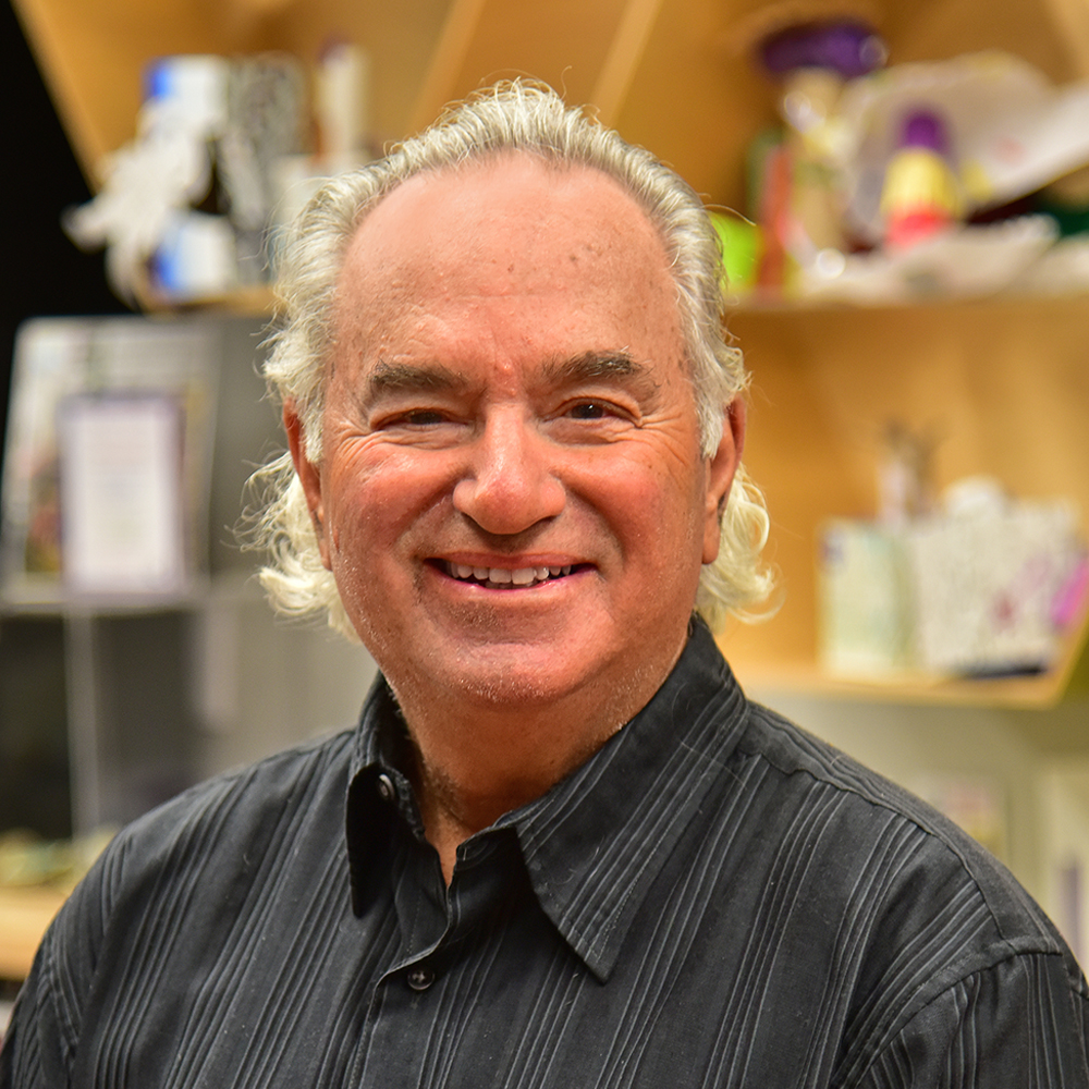 Stuart Grodin Man with white curly hair wearing black dress shirt with stripes smiling