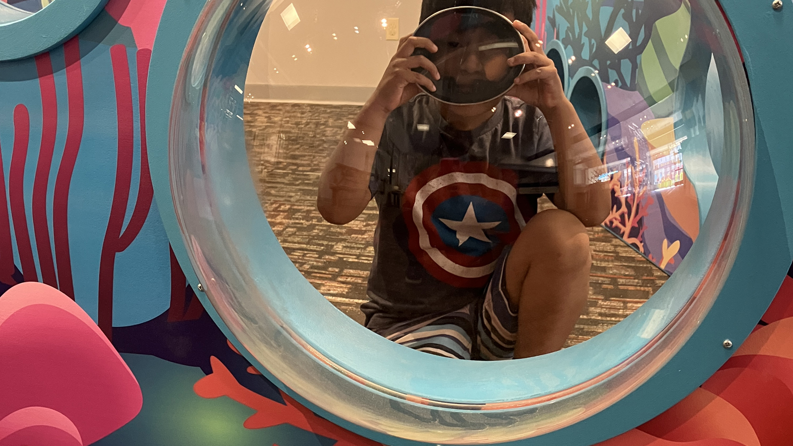 Young boy wearing scuba mask looking through a play port window with ocean decoration