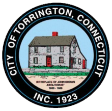 The seal of the City of Torrington, CT. A black circle with white text reading "City of Torrington, Connecticut Inc. 1923" surrounds an image of the John Brown Birthplace house.